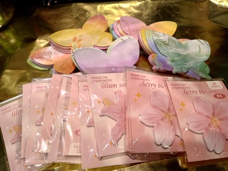 May include: A collection of butterfly-shaped sticky notes in various pastel colors and patterns, packaged in clear plastic sleeves. Each sleeve features the text Note for Sticky Notes, with labels for lilium son and cherry blossoms, including 30 sheets.