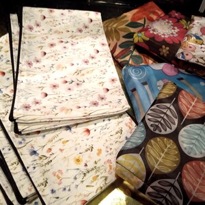 May include: A collection of rectangular fabric pouches featuring various patterns including a white background with delicate wildflowers, a dark brown base with colorful leaf motifs, a blue abstract design, and a white print with small birds.
