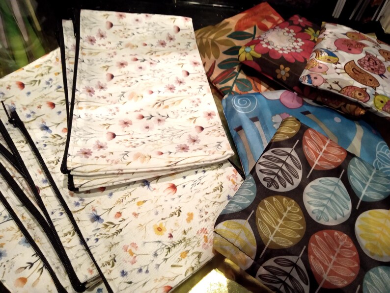 May include: A collection of rectangular fabric pouches featuring various patterns including a white background with delicate wildflowers, a dark brown base with colorful leaf motifs, a blue abstract design, and a white print with small birds.