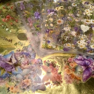 May include: A collection of transparent sticker sheets featuring botanical illustrations of daisies, purple wildflowers, and various floral arrangements. Several individual die-cut stickers display colorful butterflies surrounded by clusters of roses and blossoms.