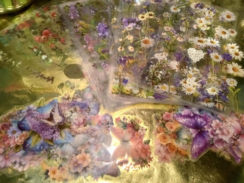 May include: A collection of transparent sticker sheets featuring botanical illustrations of daisies, purple wildflowers, and various floral arrangements. Several individual die-cut stickers display colorful butterflies surrounded by clusters of roses and blossoms.