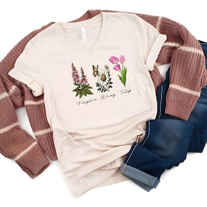 May include: A beige v-neck t-shirt with a floral design and the text "Forget-me-not Daisy Tulip".