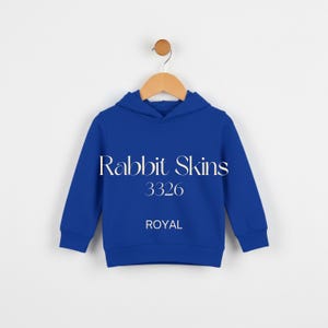 May include: A royal blue hooded sweatshirt for children, hanging on a wooden hanger. The sweatshirt features the text "Rabbit Skins 3326 ROYAL" in white. The garment is made of a soft material and is designed for comfort.