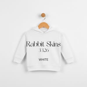 May include: A white hooded sweatshirt with the text "Rabbit Skins 3326 WHITE" in black. The sweatshirt is hanging on a wooden hanger against a white background. The garment has a ribbed hem and cuffs.