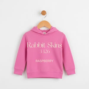 May include: A raspberry-colored hoodie with the text "Rabbit Skins 3326 RASPBERRY" printed on the front. The hoodie is hanging on a wooden hanger against a white background. The hoodie has a hood and long sleeves.