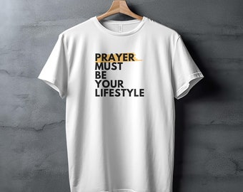 Peut inclure: T-shirt blanc avec le texte "PRAYER MUST BE YOUR LIFESTYLE" imprimé en noir, le mot "PRAYER" étant mis en évidence en or.