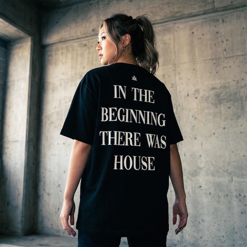 May include: A black short-sleeved t-shirt featuring white text on the back that reads IN THE BEGINNING THERE WAS HOUSE, with a small white logo above the text. The shirt has a crew neckline and a standard fit, shown from the back view.
