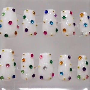 May include: Set of ten white false nails with colorful rhinestones. Each nail has a different pattern of rhinestones.