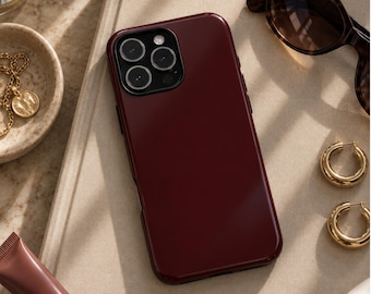 May include: A deep burgundy smartphone case with a smooth, glossy finish and a rectangular camera cutout featuring three circular lenses. The case is designed to fit a mobile device with a standard button layout on the side edges.