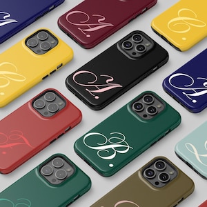 May include: A collection of colorful phone cases in various shades, including yellow, red, and green. Each case features a unique cursive initial design in contrasting colors. The cases are arranged in a diagonal pattern, showcasing their different colors and designs.