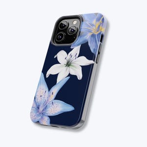 May include: A navy blue phone case with a floral pattern of white and light blue lilies. The lilies have yellow details and are set against a dark background. The case has a silver-coloured border.