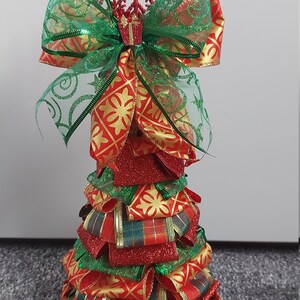 Puede incluir: Una decoración de árbol de Navidad roja y verde hecha de cinta con un copo de nieve brillante en la parte superior.
