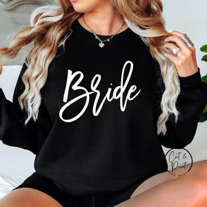 May include: Black crew neck sweatshirt with the word "Bride" in white script lettering. The image also includes the logo for "Cat & Print SVG Shop".