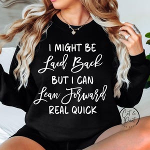 以下が含まれることがあります： 「I MIGHT BE Laid Back BUT I CAN Lean Forward REAL QUICK」の白文字がプリントされた黒いスウェットシャツ。長袖でクルーネックです。画像には「Cut & Print SVG SHOP」のロゴも含まれています。