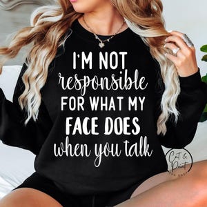 May include: Black sweatshirt with the text "I'M NOT responsible FOR WHAT MY FACE DOES when you talk" in white script. The sweatshirt has long sleeves and a crew neck. The image also includes the "Cut & Print SVG SHOP" logo.