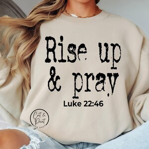Puede incluir: Una sudadera beige con el texto "Rise up & pray" en negro, con la referencia bíblica "Lucas 22:46" debajo.