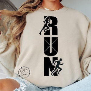 Könnte beinhalten: Ein beiger Pullover mit einem schwarzen grafischen Design, das "RUN" sagt, mit einer Silhouette eines Läufers für jeden Buchstaben.