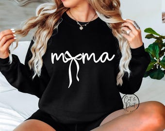 Puede incluir: Sudadera negra con la palabra "momma" en escritura blanca y un diseño de lazo. La sudadera es de cuello redondo. La imagen también incluye el logotipo "Cat & Print SVG Shop".