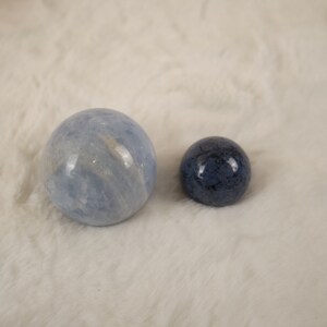 May include: Two polished spheres, one light blue and one dark blue, on a white fuzzy surface.