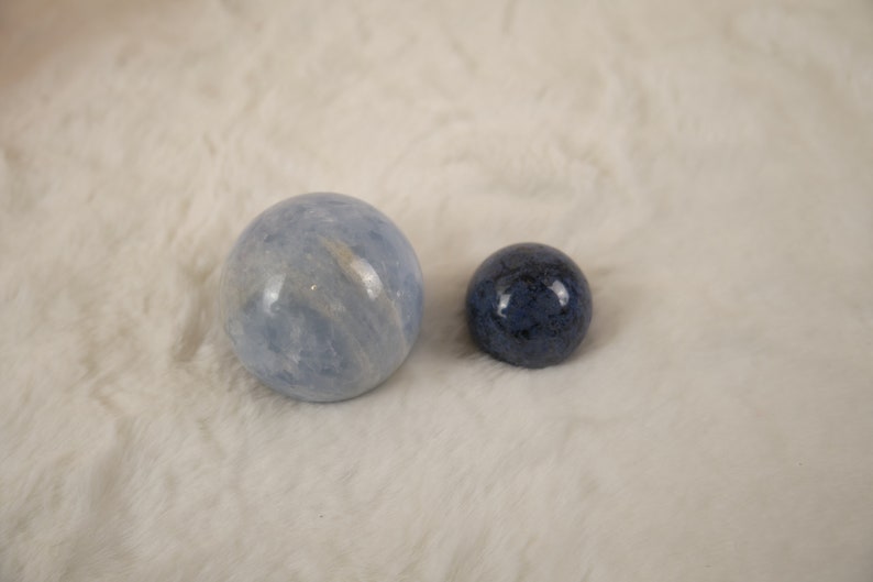May include: Two polished spheres, one light blue and one dark blue, on a white fuzzy surface.