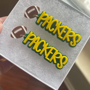 May include: Green and yellow 'Packers' earrings with a brown and white football charm.