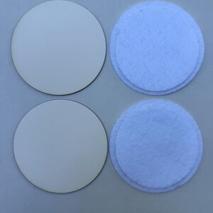 May include: Four round coasters. Two are made of light-colored wood, and two are light blue felt. The coasters are arranged in a square formation, with the wood coasters on the left and the felt coasters on the right.