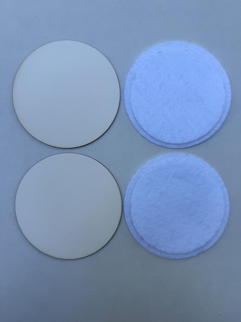 May include: Four round coasters. Two are made of light-colored wood, and two are light blue felt. The coasters are arranged in a square formation, with the wood coasters on the left and the felt coasters on the right.