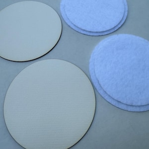 May include: Two light beige wooden circles and two stacks of light blue felt circles are arranged on a gray surface. The wooden circles have a dark brown edge. The felt circles are stacked in pairs.