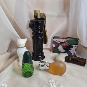 May include: A collection of vintage glass items including a white cat figurine, a tall black glass bottle with a brass-coloured metal top, a green textured glass bottle, a frosted amber glass hippo, and a Mini-Derringer box with a toy pistol.