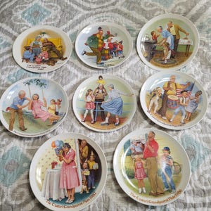 Puede incluir: Una colección de ocho platos decorativos con ilustraciones coloridas de escenas familiares. Cada plato tiene un borde blanco y texto en la parte inferior, como "The Cszari Grandparent Plate 1980". Los platos representan diversas actividades familiares.