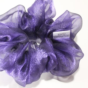 Op de afbeelding: Een paarse, glinsterende haarband met een wit label waarop "ZOLAWYRE GIFTS" staat.