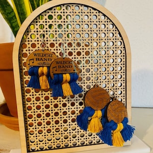 May include: Two pairs of earrings with wooden charms and blue and yellow tassels. The charms are round and feature the text "Wildcat Band" and a musical note. The other pair of earrings feature a basketball design.