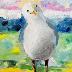 Op de afbeelding: Een witte meeuw met een gele snavel staat op een geel en groen grasveld met een blauwe en paarse lucht op de achtergrond.