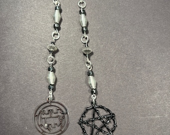 May include: A silver chain with black beads and two charms. One charm is a silver circle with a geometric design. The other charm is a black pentagram.