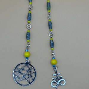May include: A silver chain with gray and yellow beads, a silver pendant with a web design, and a silver pendant with a snake wrapped around a cross.
