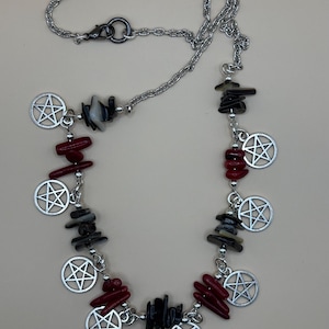 May include: A silver chain necklace with red coral and black stone beads. The necklace has multiple silver pentagram charms.