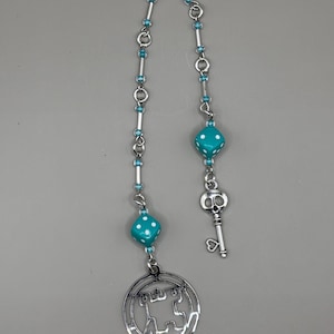 May include: A silver chain with a teal blue dice charm, a silver key charm, and a silver circular charm with a stylized design.