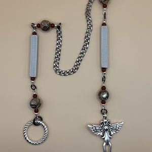 May include: A silver chain with brown and green beads, two silver rectangular charms, a silver ring, and a silver pendant with an angel wing design.
