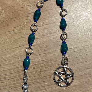 May include: A silver chain with teal and blue beads, a silver pentacle charm, and a silver goddess charm.
