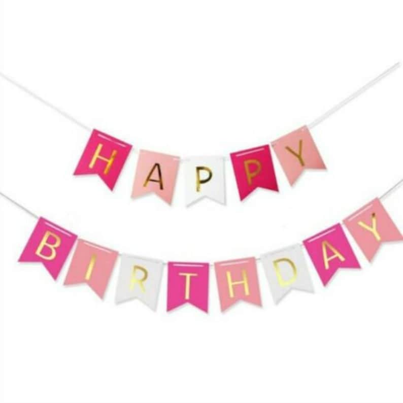May include: A festive banner with the words "HAPPY BIRTHDAY" in gold lettering. The banner features pink, white, and light pink pennant flags strung on a white string, perfect for birthday celebrations.