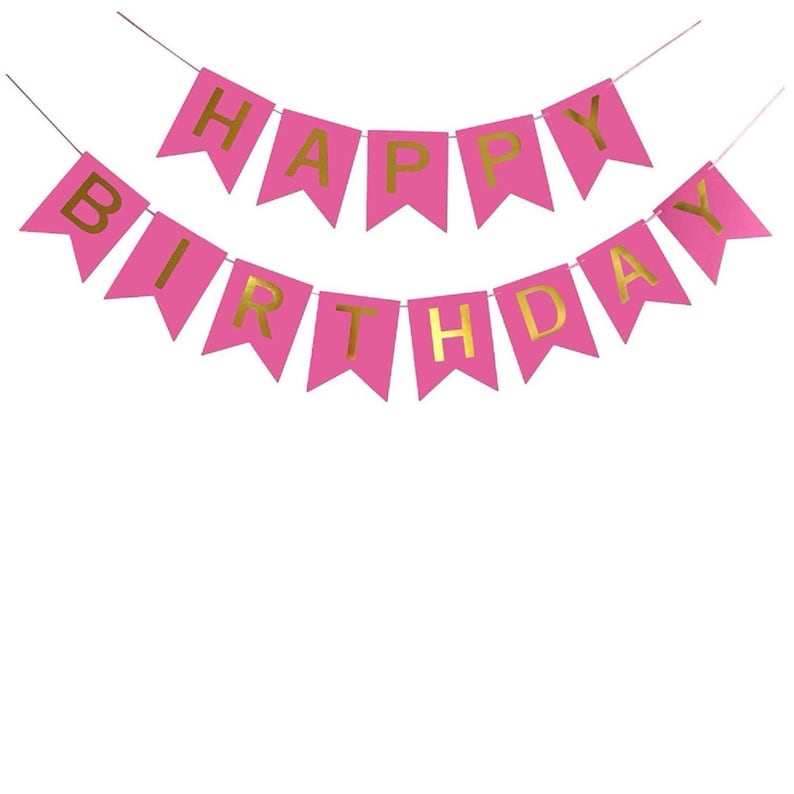 May include: Pink banner with gold lettering spelling "HAPPY BIRTHDAY". The banner is strung on a thin white string. The banner is a festive decoration for a birthday celebration.