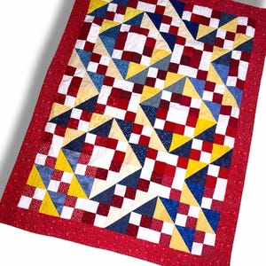 May include: A rectangular quilt featuring a patchwork design of red, white, yellow, and blue fabric squares. The pattern consists of alternating blocks of small checkered squares and larger triangles, all enclosed within a solid red border.