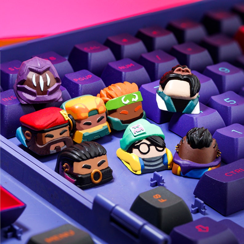 Pode incluir: Um conjunto de oito teclas coloridas com diferentes personagens e designs. As teclas s&atilde;o de pl&aacute;stico e t&ecirc;m um acabamento brilhante. As teclas est&atilde;o dispostas em um teclado com teclas pretas e um fundo roxo.