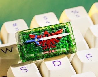 May include: A green, clear, resin keycap with a red and blue sword and shield design. The keycap is on a white keyboard with the letters W, S, D, F, and C visible.
