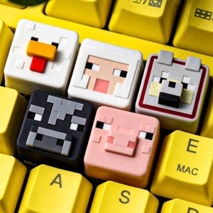 Puede incluir: Cinco teclas mecánicas cuadradas con caras de animales pixeladas, incluyendo un pollo blanco con cresta roja, una oveja blanca, un lobo gris, una vaca negra y un cerdo rosa, colocadas sobre un teclado de computadora de color amarillo brillante.