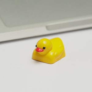 Puede incluir: Un juguete de pato de goma amarillo con un pico rojo y ojos negros. El pato est&aacute; acostado de lado con la cabeza levantada.