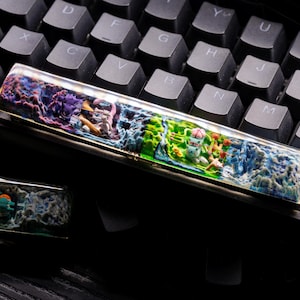 May include: A colorful keyboard keycap with a 3D design featuring a whimsical scene with a small house, trees, and flowers. The keycap is made of clear resin and has a glossy finish.