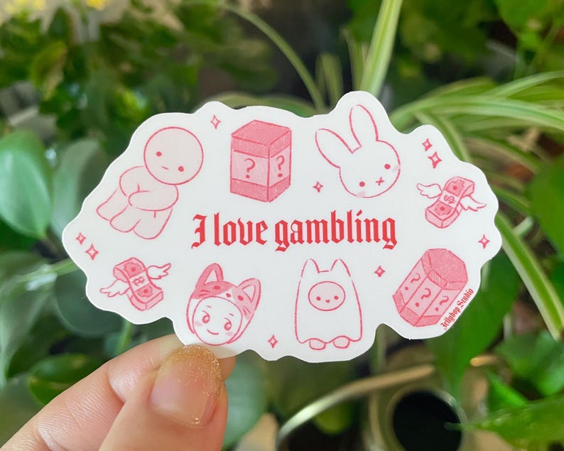 以下が含まれることがあります： ピンクと白のステッカーに「ギャンブルが好き」というテキストと、ウサギ、お金袋、サイコロ、帽子をかぶったキャラクターなど、さまざまなイラストが描かれています。