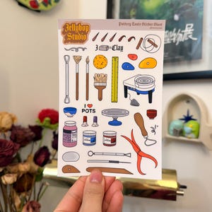 May include: A sticker sheet featuring pottery tools and the text "Jellybob Studio." The illustrations include tools like brushes, pottery wheels, and jars. The words "I love POTS" are also visible on the sticker sheet.