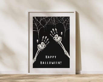 May include: A white framed print with a black background featuring two white handprints with skeletal arms reaching up. The handprints are surrounded by white spiderwebs. The text "Happy Halloween!" is printed in white at the bottom of the print.